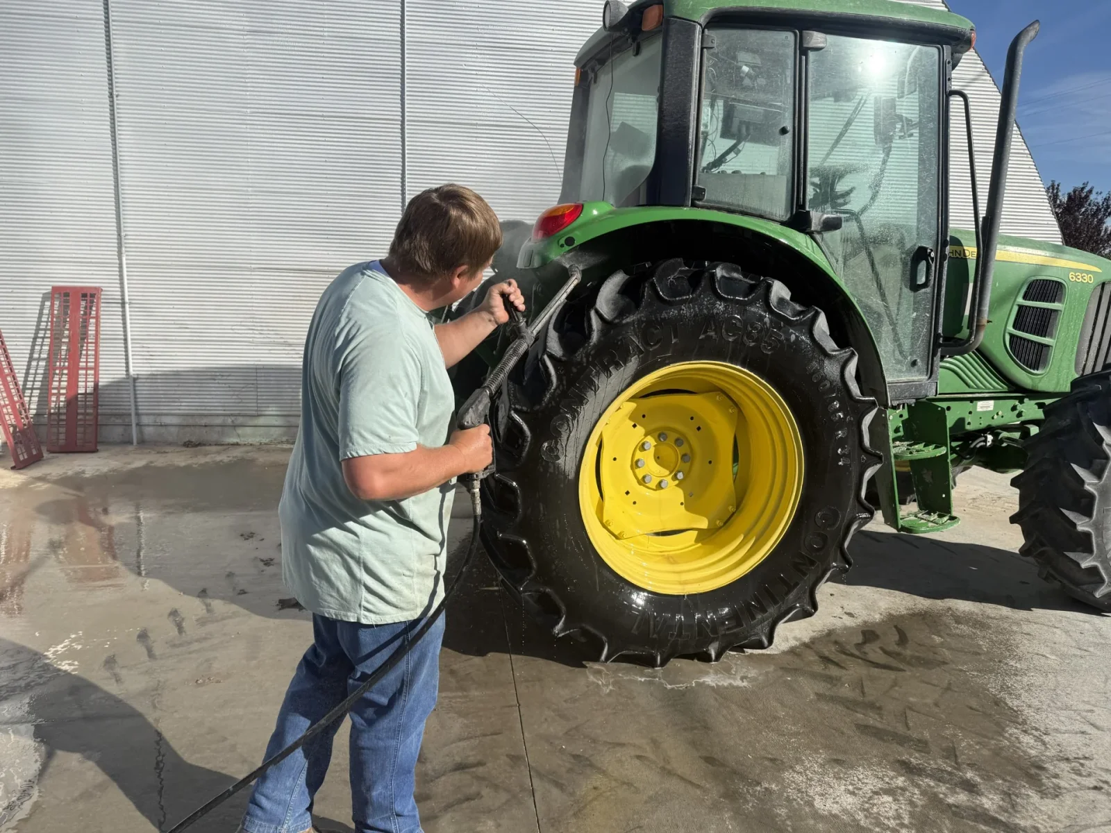 Person pressure-washing a tractor's rear tire to clean field equipment.